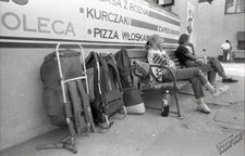 Dworzec PKS w Lublinie - podr&oacute;żni oczekujący z plecakami na ławce przy ścianie budynku dworca